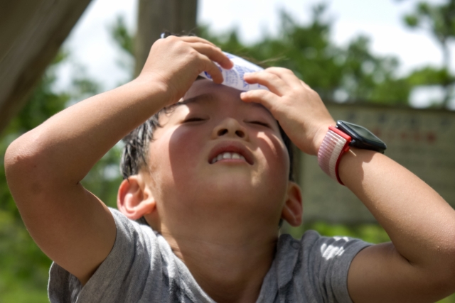 炎天下で汗をぬぐいながら暑さに耐える子ども